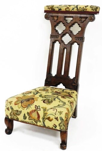 A Victorian Gothic oak prie dieu chair, with padded top and seat, on compressed sabre back and scroll front legs, with a heavily carved partially pierced back, raised by floral roundels, 86cm high.