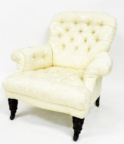 An Edwardian deep seated armchair, with button back, shaped arms, and deep seat, on turned front and sabre back legs terminating in castors, in later floral material, 85cm high.
