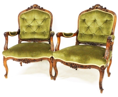 A pair of French salon style carver chairs, each with button backs, overstuffed arms and serpentine seats, on heavily carved front legs, with carved frames, 95cm high. (2)
