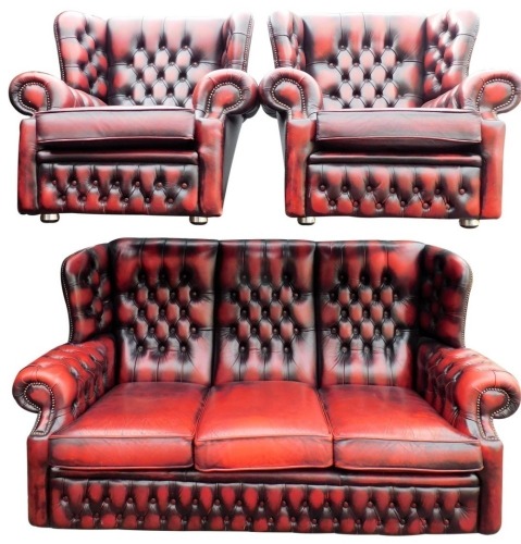 A club style three piece suite, in red leatherette, comprising three seater wing settee and two wing armchairs, each overstuffed in button back red leatherette, the armchairs 92cm high.