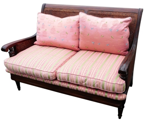 A 20thC two seat bergere salon settee, in the manner of Waring & Gillow, with shaped scroll arms on turned legs, with associated cushions, 128cm wide.