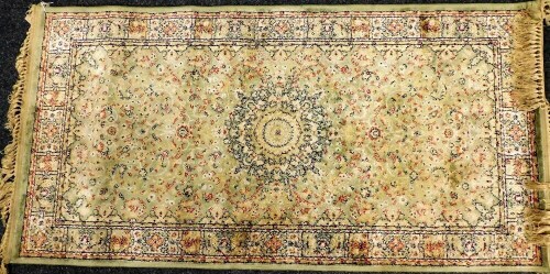 A Persian green ground rug, decorated with a central medallion and arabesque's, within a repeating floral border, 151cm x 76cm.