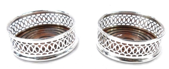 A pair of silver wine coasters, with a rounded wooden base and pierced fret border, Birmingham 1986, 9cm diameter, 3&frac12;oz all in.