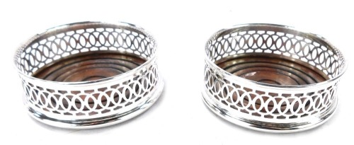 A pair of silver wine coasters, with a rounded wooden base and pierced fret border, Birmingham 1986, 9cm diameter, 3&frac12;oz all in.