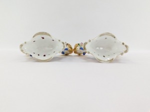 A pair of early 19thC Fischer & Mieg porcelain cornucopia vases, each encrusted with flowers and centred with a seated figure of a girl flower seller, raised on a naturalistic ground and rococo scroll base, one stamped CF324, the other F&M, 22cm wide. (AF - 6