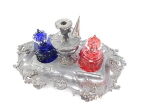 A Victorian silver plated desk stand, embossed with rococo scrolling leaves and dolphin's heads, with a central taper stick lidded mixing bowl, flanked by a pair of Gothic glass inkwells, one in cobalt blue, the other in ruby red, raised on scroll feet, 3 - 2
