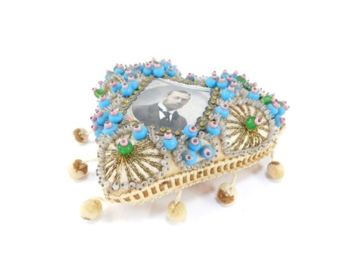 A George V Coronation sweetheart pin cushion, 20thC with a portrait of The King, and 'With Best Wishes' to the shoulders, otherwise decorated with wirework and beading, 16cm wide.
