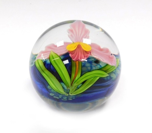 A Mayauel Ward paperweight, decorated with a pink orchid, against a mottled blue ground, etched signature, dated 2011, serial no PW42POS, 7cm diameter.