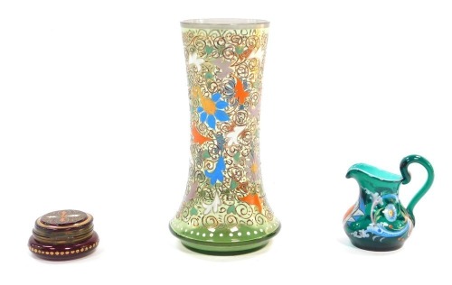 An early 20thC Bohemian green glass vase, enamel decorated with scrolling flowers and leaves, 17.5cm high. ruby glass rouge pot and hinged cover, with enamelled leaf decoration, and a turquoise glass cream jug, enamel decorated with a coat of arms and ro