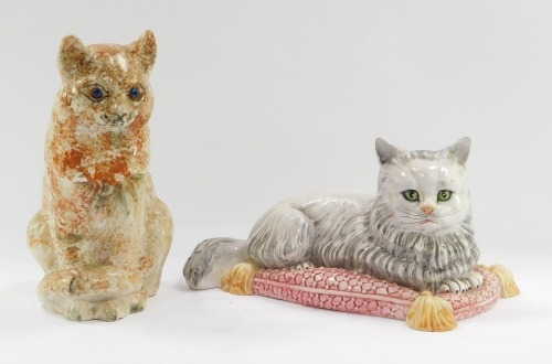 Two pottery cat figures, comprising an Italian recumbent cat on a pink cushion, 31cm wide, No A/7480, and a further seated example unmarked, 26cm high. (2)