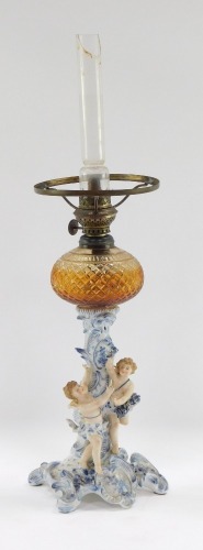 A Continental porcelain cherub oil lamp, the amber glass faceted reservoir on a blue and white porcelain stem with two cherubs, with a glass funnel, 37cm high. (AF)