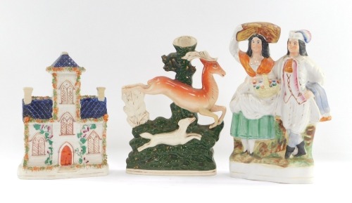A group of Staffordshire flat back figures, comprising a Staffordshire flat back cottage, 25cm high, a spill vase with deer and greyhound, 25cm high, and a two person figure group. 28cm high. (3)