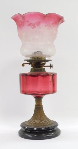A Victorian cranberry glass oil lamp, the flared shade with etched floral detail and a cranberry glass reservoir, on brass stemmed base with ebonised knop ends, 48cm high overall.