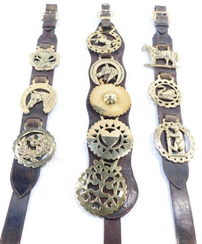 Three brown leather martingales, each with applied horse brasses, of varying design.