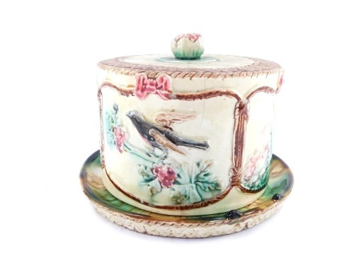 A late 19thC French majolica cheese dish and cover, the circular top with panelled bird and floral detail and water lily finial, on a moulded base, 15cm high, 22cm wide.
