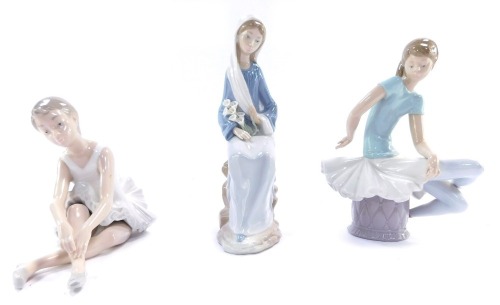 Three Lladro and Nao figures, comprising a Lladro figure of a seated ballerina, 21cm high, a Nao figure of a stretching seated ballerina, 13cm high, and a Lladro figure of a lady perched on a rock, carrying calla lillies, 24cm high. (3, AF)