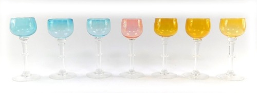 A set of seven coloured wine glasses, three blue, three green and one pink, on a clear glass stem with frilled knop, etched to foot K T Q Oylan. '75, each 19cm high. (7)