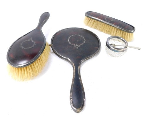 A silver and tortoiseshell dressing table set, with Neo Classical pique central wreath motif, comprising two brushes and a hand mirror, hallmarks worn, together with an Edward VII silver rimmed glass salt cellar, London 1907, with plated mustard spoon. (5