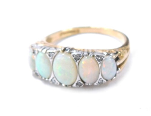 A 9ct gold opal and diamond dress ring, the setting set with five oval opals and eight tiny diamonds, with scroll and ribbed design shoulders, size O, 3.6g all in, boxed.