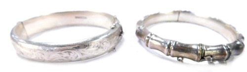 Two silver bangles, comprising a Victorian half hinged foliate scroll bangle, with safety chain, and another of shaped form, 37.2g all in. (2)