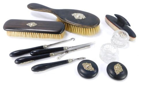 An early 20thC ebony dressing table set, comprising hand brush, dressing table brush, two dressing table jars, a buffer, nail clips, glove stretchers, etc., some with applied white metal foliate detail. (a quantity)