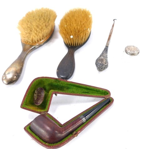 A group of silver dressing table jewellery, comprising a wooden handled and scroll silver inset hand mirror, a white metal handled hairbrush, white metal topped cut glass smelling salt jar, a silver collar Astoria gentleman's pipe in fitted case, and a wh