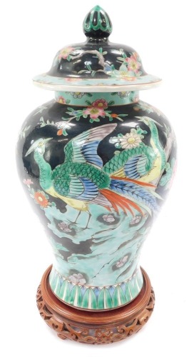 A Chinese Republic famille noir porcelain vase and cover, of baluster form, decorated with pheasants, prunus blossom and peonies, printed mark, 32cm high, with a carved wooden stand.