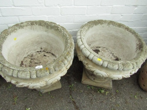 A pair of reconstituted stone planters, each with ribbed and foliate scroll detail, 51cm high, 52cm diameter.
