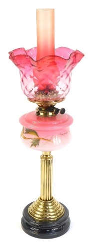 A Victorian cranberry glass oil lamp, with a cranberry glass flared shade and chimney, and a painted floral reservoir on brass column with ebonised base, 71cm high.