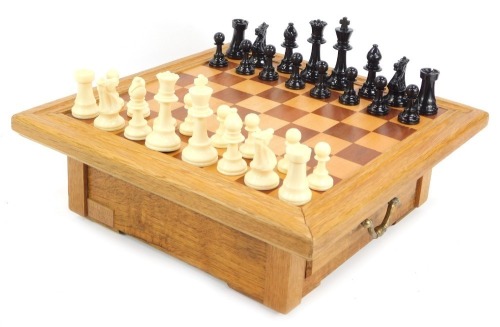 A teak chess board, with moulded top and two drawers for pieces, with high gloss chess pieces, the knight 10cm high.