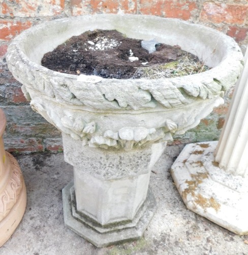 A reconstituted stone planter, the bowl with leaf moulded and applied fleur de lis decoration on an associated octagonal base, 63cm high, 57cm diameter.