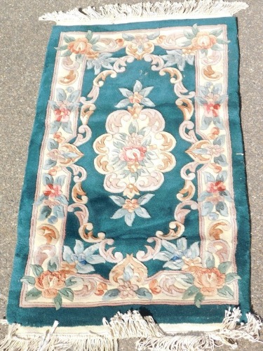 A Chinese rug, green ground decorated centrally with floral medallion, within a surround of flowers, 117cm x 69cm.