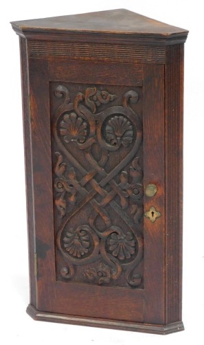 A 19thC oak corner cupboard, with central carved shell panel, with brass handle, 64cm high, 37cm wide, 22cm deep.