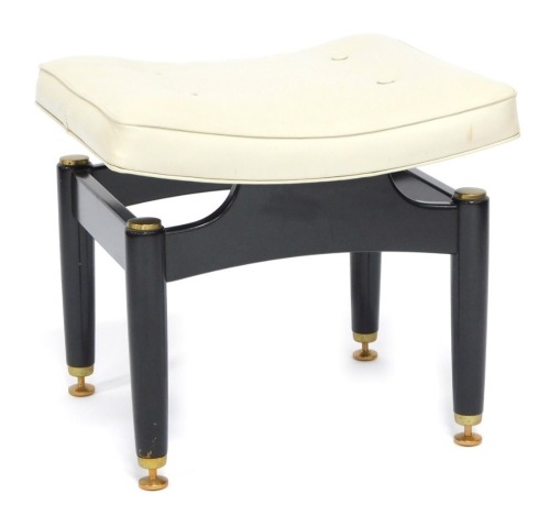 A 1950's G-Plan ebonised and brass stool designed by E Gomme, with a cream leatherette padded seat, 48cm wide. The upholstery in this lot does not comply with the 1988 (Fire & Fire Furnishing) Regulations, unless sold to a known exporter or upholsterer it