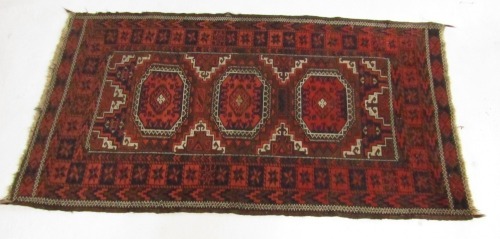 A Belouch rug, red ground, decorated with three central medallions, within repeating floral borders, 151cm x 86cm.