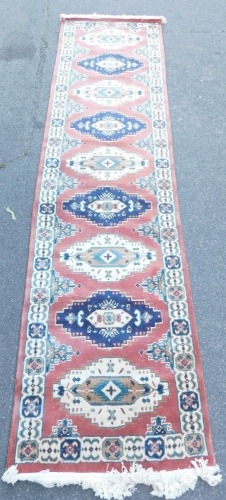 A Persian style runner, red ground decorated with nine cream and blue ground medallions, within repeating floral borders, 324cm x 81cm.